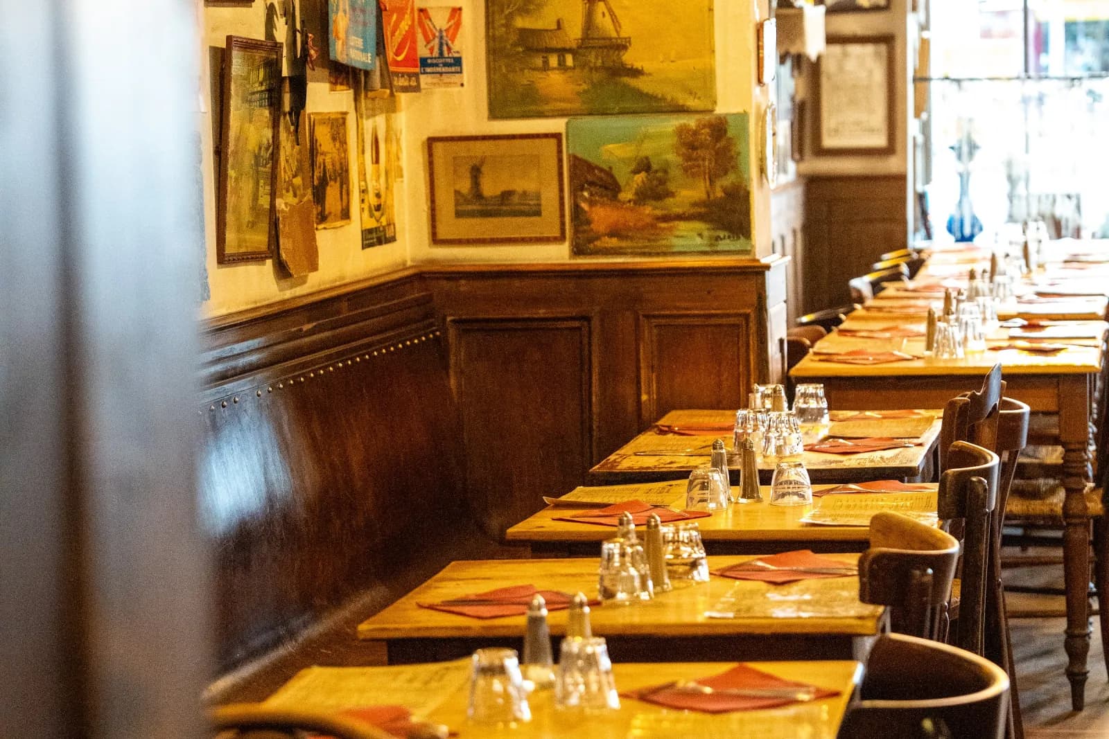 De zaal met gele muren, twee rijen houten tafels en bistrostoelen op een rij.