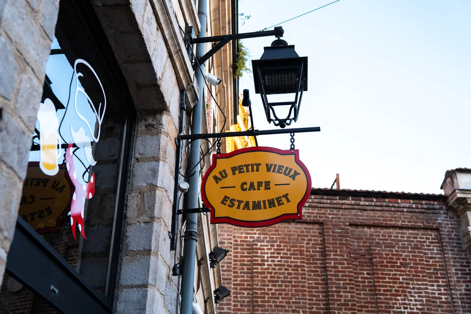 El letrero redondo de Au Petit Vieux, « café estaminet », colgado bajo un farol en la place aux Oignons.