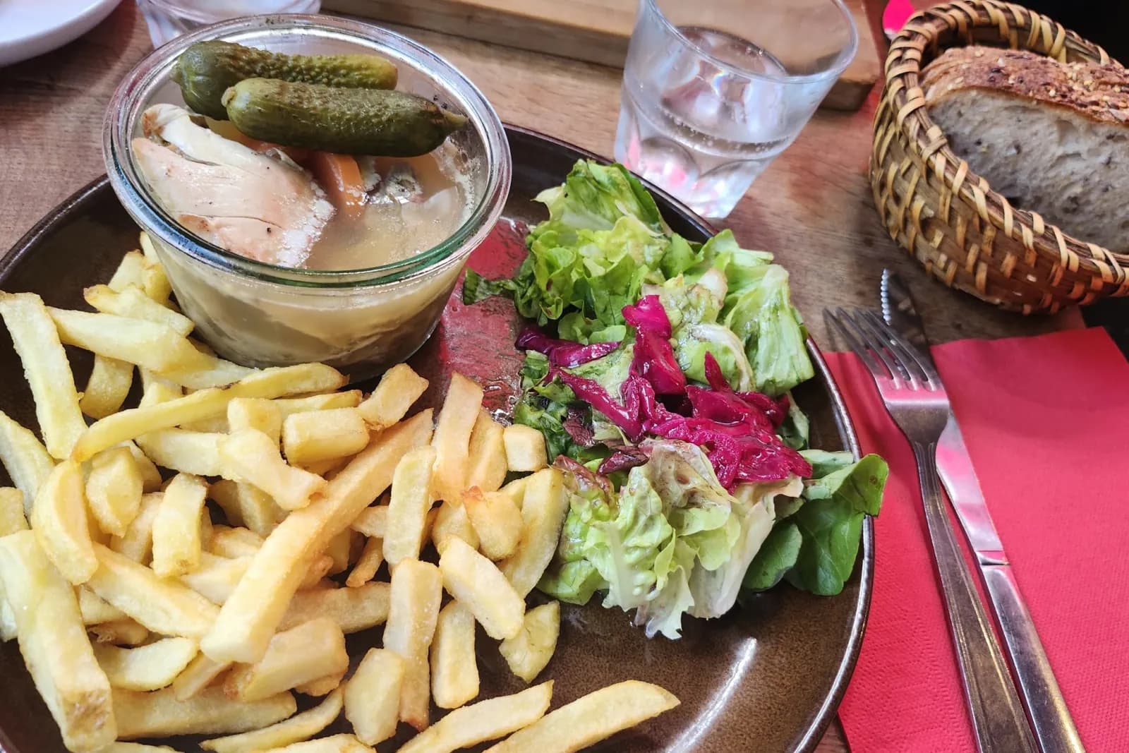 Un potjevleesch servi dans son bocal avec des cornichons, des frites fraîches et une salade.