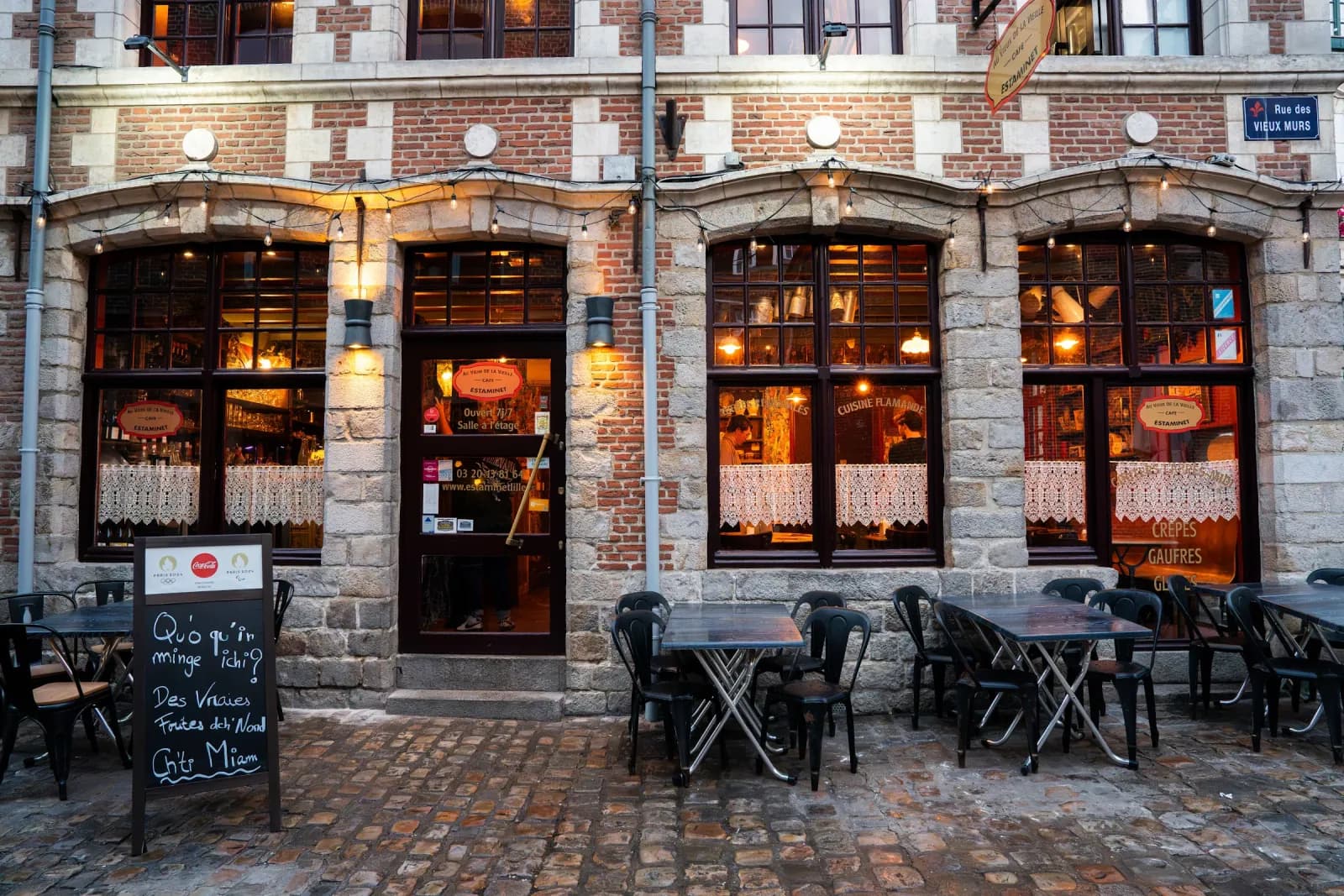 The brick and white stone front of Au Vieux de la Vieille, rue des Vieux Murs, lit windows and terrace on the cobbles.